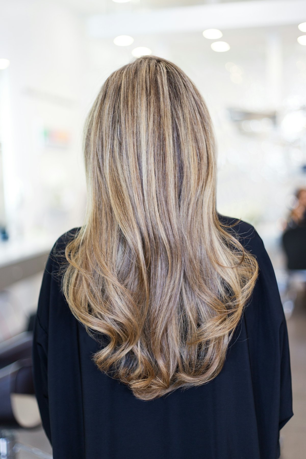 ハイライトを入れた、毛先にゆるいカールのあるロングヘアの後ろ姿